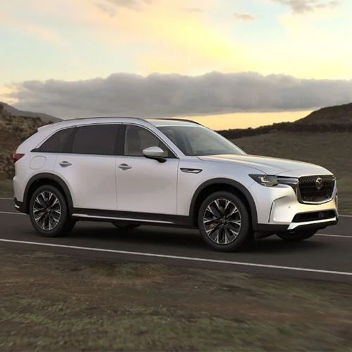 CX-90 PHEV drives down secluded dusty highway at sun down.  