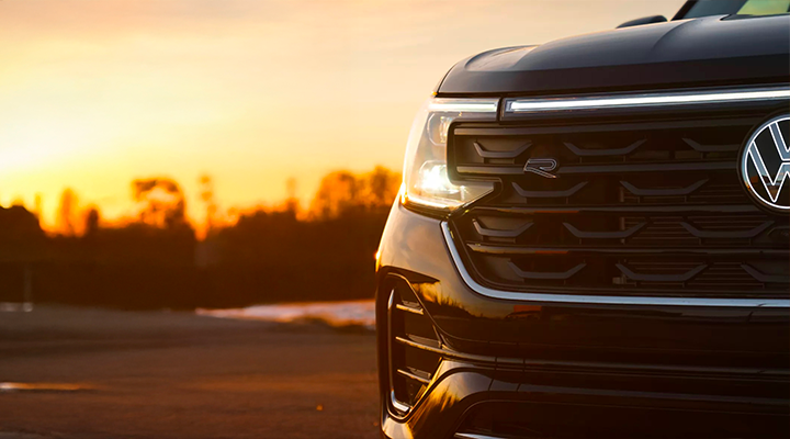 Gros plan sur la calandre avant et le phare à DEL d'un Volkswagen Atlas noir au coucher du soleil, mettant en évidence l'emblème R.