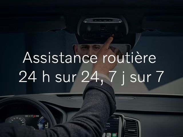 Depuis le siège du conducteur, une personne tend la main pour appuyer sur le bouton « SOS » de la console au pavillon d'une Volvo. Le texte « Assistance routière 24 h sur 24, 7 j sur 7 » est superposé sur l'image.