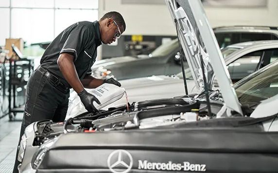 Mechanic pouring fluid into a car engine at a Mercedes-Benz dealership.