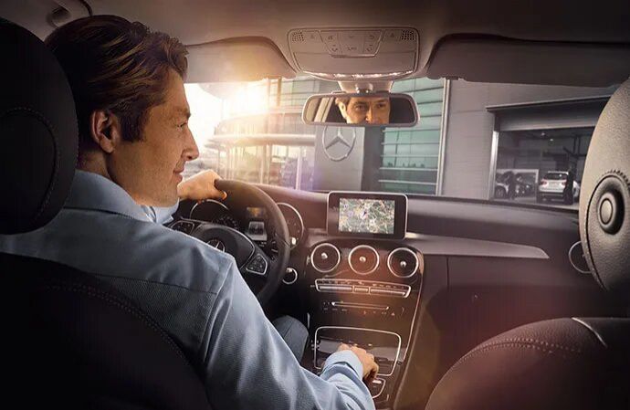 Interior view of a Mercedes-Benz with a man driving and using the dashboard display screen.