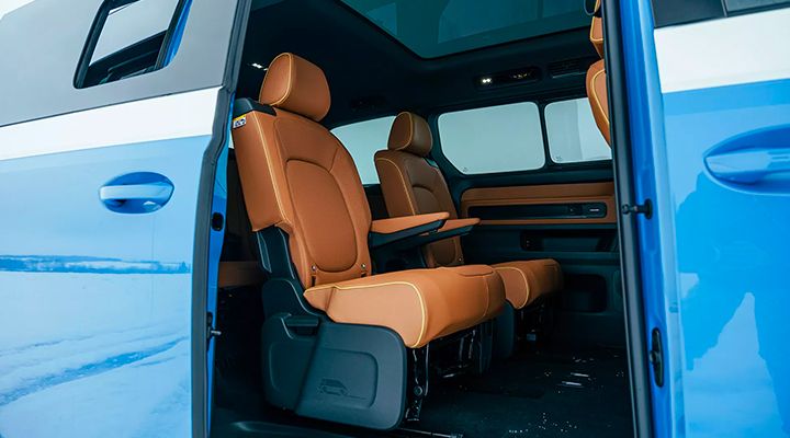 Vue de l'intérieur arrière d'une voiture avec la porte coulissante ouverte, montrant les sièges marron et le toit vitré.