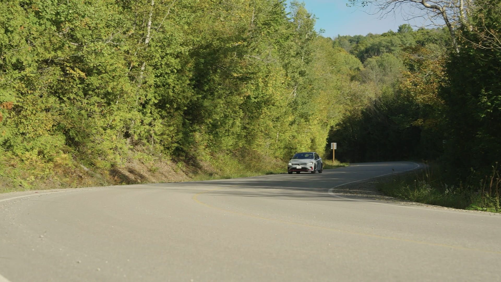 Front view of the Jetta GLI driving on a winding road surrounded by greenery.
