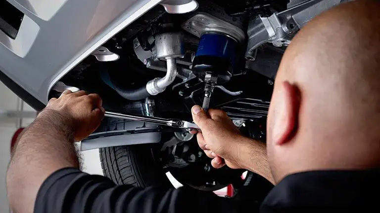 A mechanic, seen from over the shoulder, working underneath a vehicle with a socket wrench.
