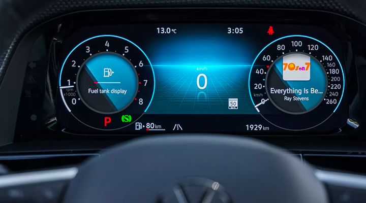 Digital instrument cluster displaying the tachometer, fuel gauge, speedometer, trip info, and current radio station details.