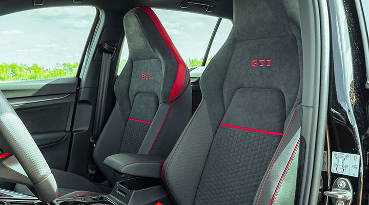 Close-up of the Golf GTI's front sport seats, featuring integrated headrests, a honeycomb pattern, and red accents.