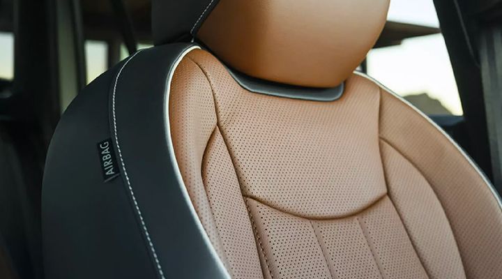 Close-up of the vehicle's front seat, highlighting the perforated brown (cognac) leather with black accents, white stitching, and the "AIRBAG" tag.