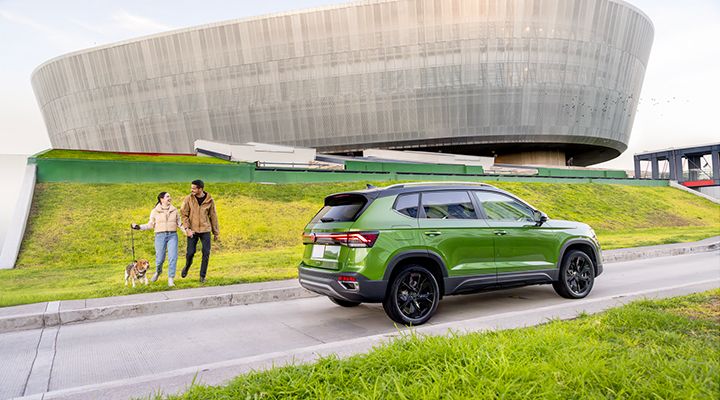 Vue arrière latérale du Taos 2026 de Volkswagen stationné sur l’herbe avec un couple à proximité, mettant en avant le démarrage à distance.
