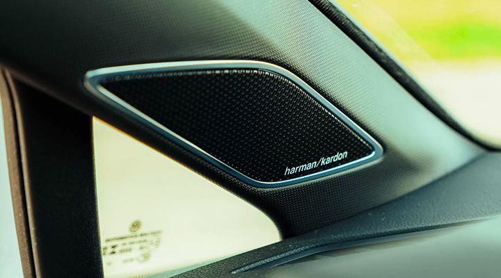 Close-up of a Harman Kardon audio speaker grille located on the A-pillar or dashboard of a car.