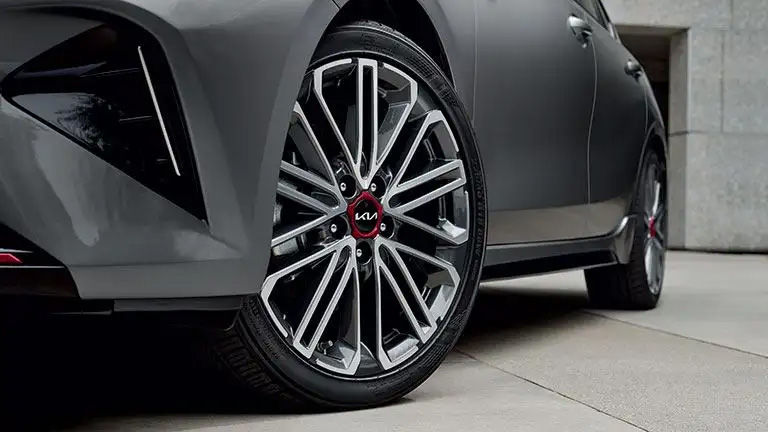 A close-up of a multi-spoke alloy wheel with a red Kia logo in the center, on a dark grey Kia Forte.