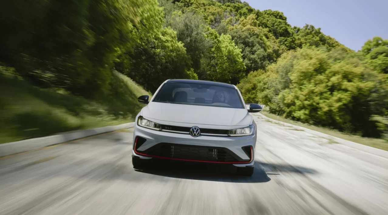 Front view of the Jetta GLI driving on a winding road surrounded by greenery.