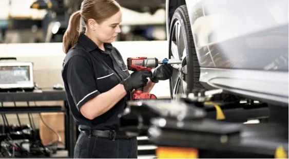 Female mechanic using a power tool on a car wheel elevated on a lift.