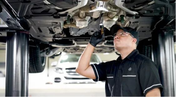 Mechanic wearing safety glasses inspecting the underbody of a car with a flashlight.