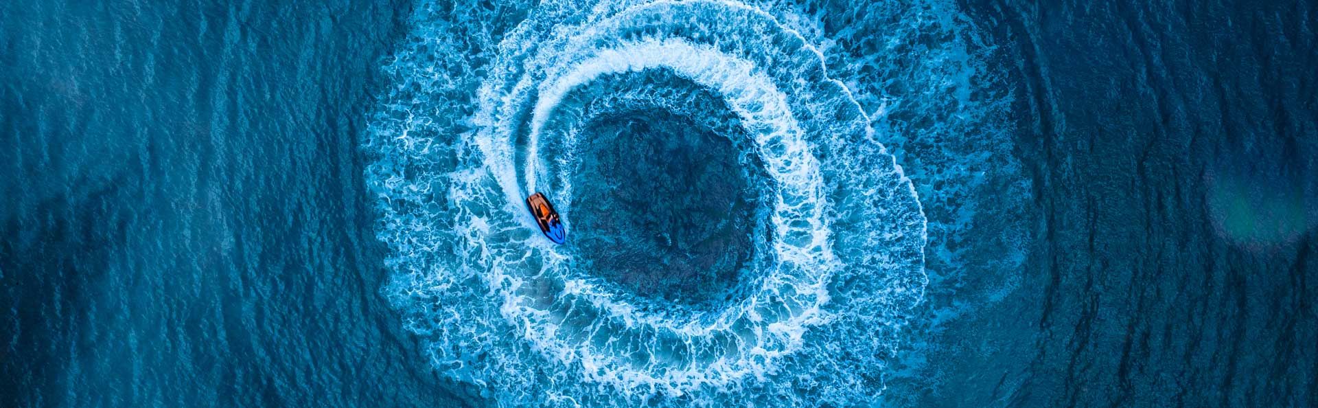 Wide shot of three jet skis speeding across blue ocean water.