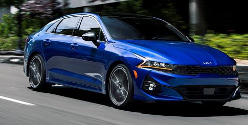 A blue Kia K5 sedan driving on a street.
