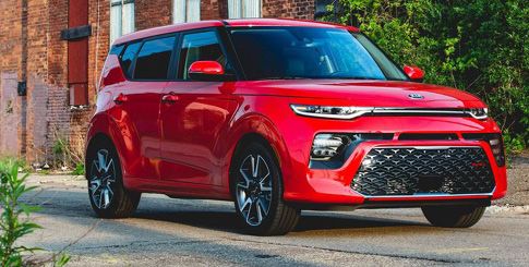 A red Kia Soul parked in front of a brick building.