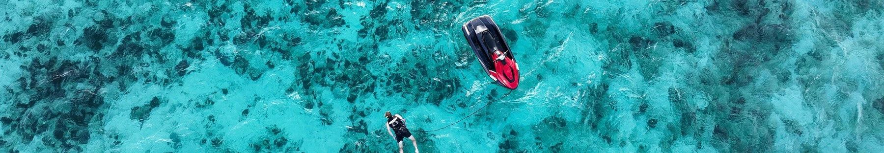 Aerial view of a red and black jet ski on clear turquoise water.	