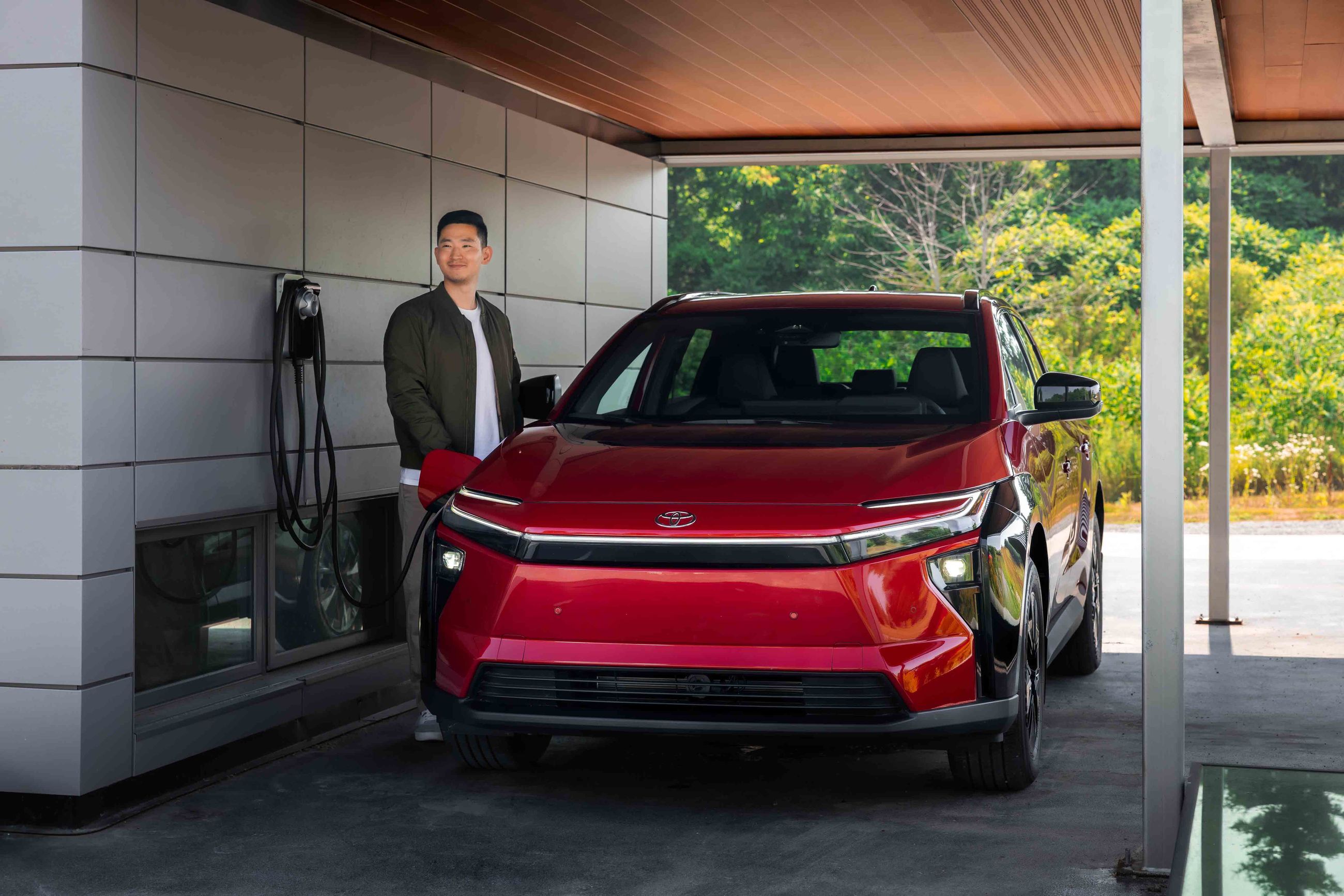 Smiling man wearing a red blazer, standing in a car dealership showroom.