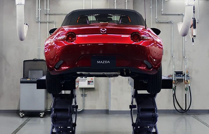 A rear view of a red Mazda MX-5 Miata raised on a hydraulic lift inside a clean, professional service bay.