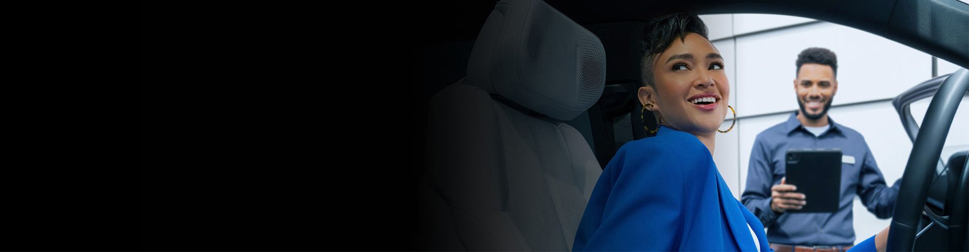 A woman in a car interacting with a service professional holding a tablet.