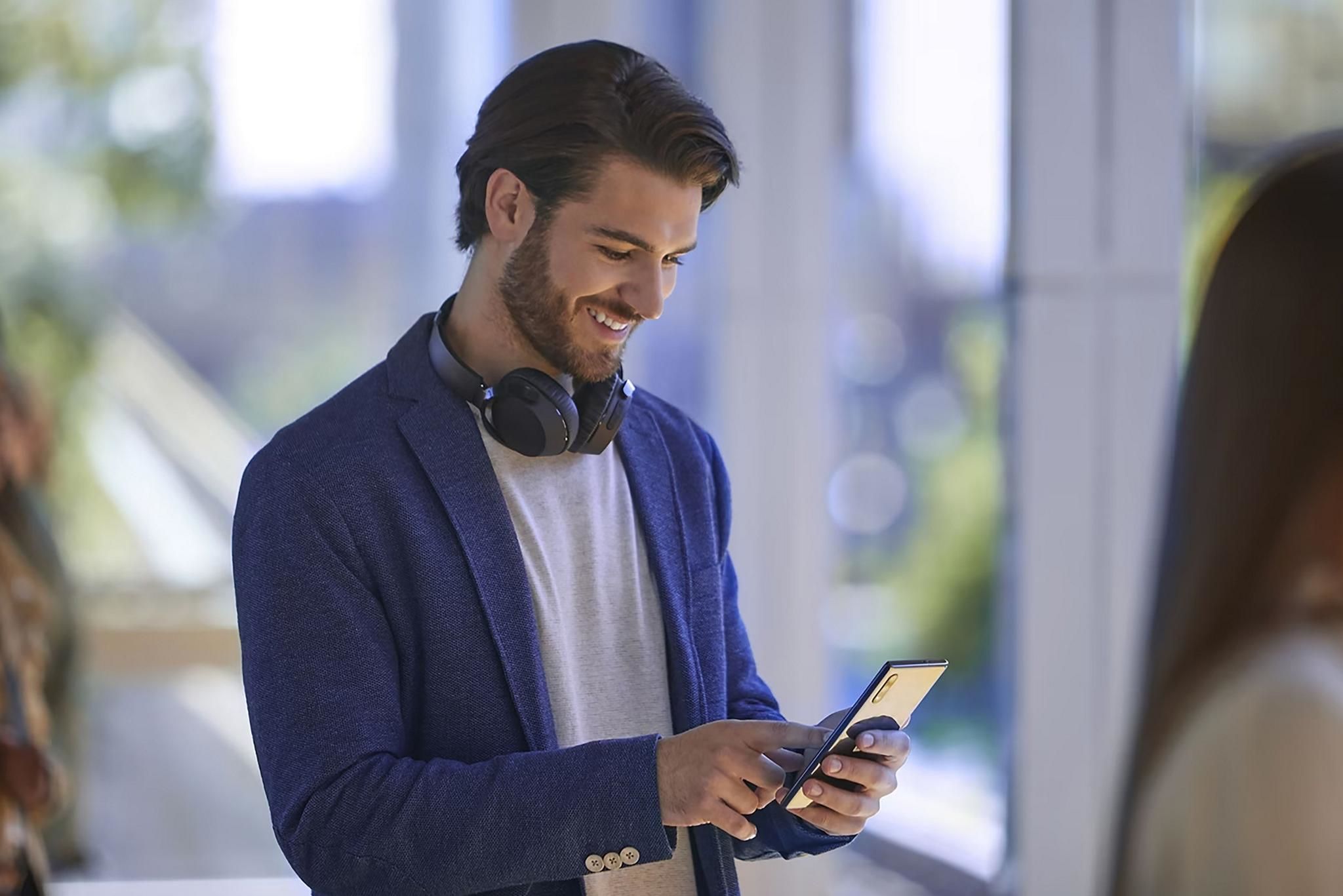 Smiling man in a blue blazer with headphones around his neck looking at his smartphone