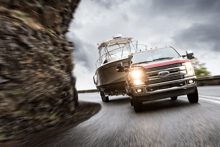 Un camion rouge Ford Super Duty circulant sur une route de montagne sinueuse tout en remorquant un grand bateau de plaisance.