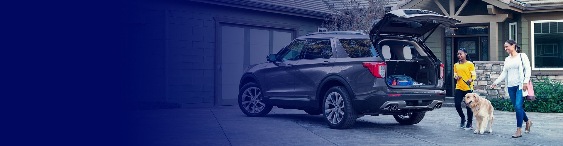 amily with a dog loading luggage into the open trunk of a Ford Explorer SUV in a driveway.