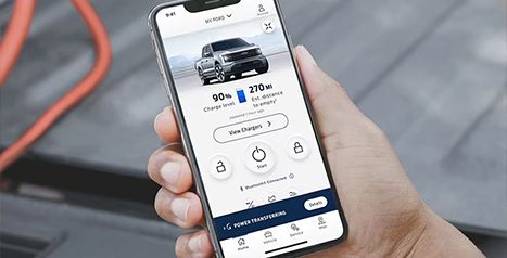 Close-up of a hand holding a smartphone with the FordPass app displayed, showing a 90% charge level and 270 miles of range for a Ford F-150 Lightning.