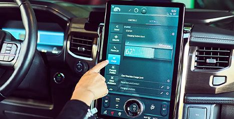 Close-up of a person's finger using the large vertical touchscreen inside a Ford F-150 Lightning to adjust charging settings.