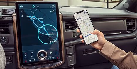A person holding a smartphone showing a map of charging stations, synchronized with the Ford vehicle's large navigation screen.