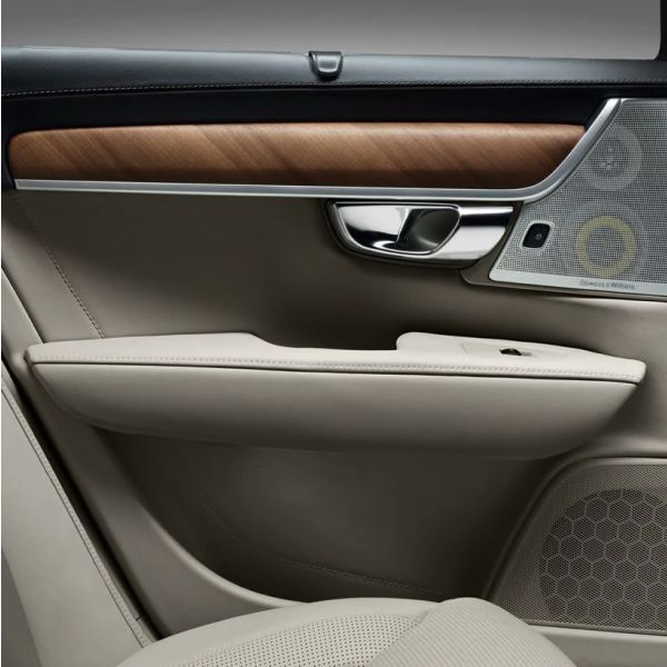 A close-up of a luxury car's interior door panel, featuring beige leather, a wood trim inlay, a chrome handle, and a Bowers & Wilkins speaker.