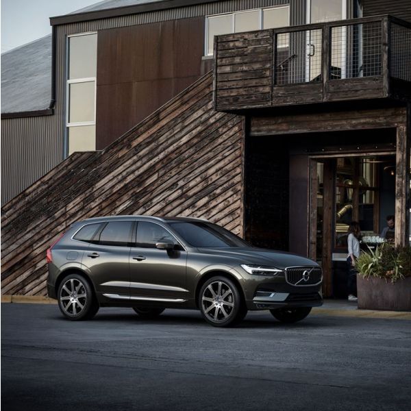 A dark grey Volvo XC60 SUV parked on pavement in front of a modern building with dark wood and metal architecture.