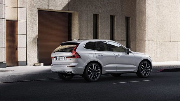 The rear-quarter view of a silver Volvo XC60 R-Design SUV parked on an urban street next to a modern building.