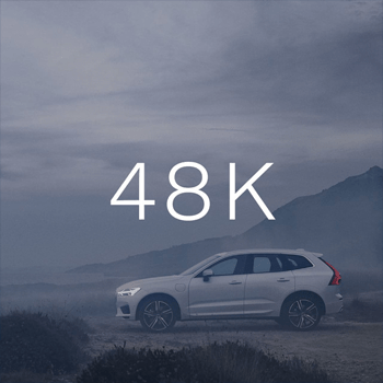 A white SUV is parked in a rugged, outdoor setting with mountains in the background under a cloudy sky, with "48K" text overlaid.