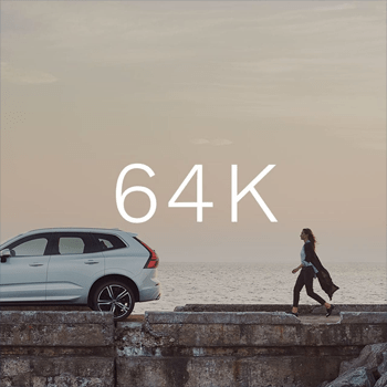 A white SUV is parked on a stone pier by the sea, as a woman walks away from it at dusk, with "64K" text overlaid.