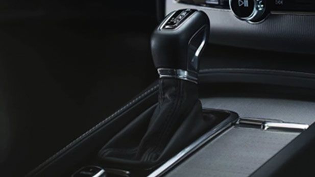 A close-up of a modern, leather-wrapped automatic gear shifter inside a Volvo, set against a brushed metal center console.