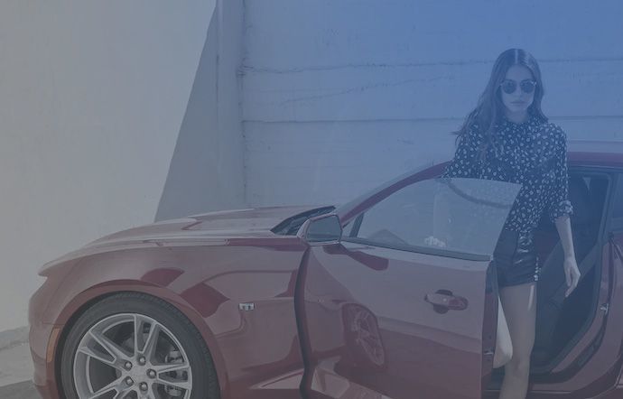 Stylish woman wearing sunglasses getting into a red sports car.