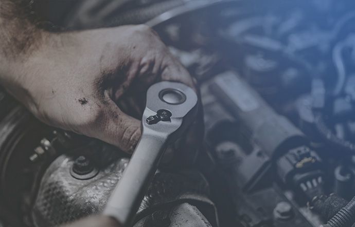 Close-up of a mechanic's hands using a ratchet wrench inside a car engine.