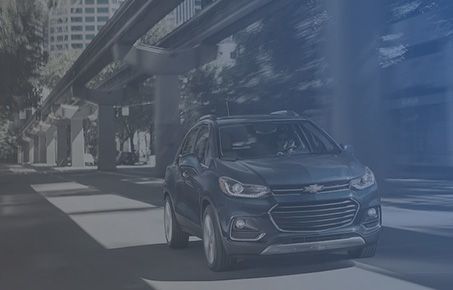 Dark Chevrolet SUV driving beneath an urban overpass.